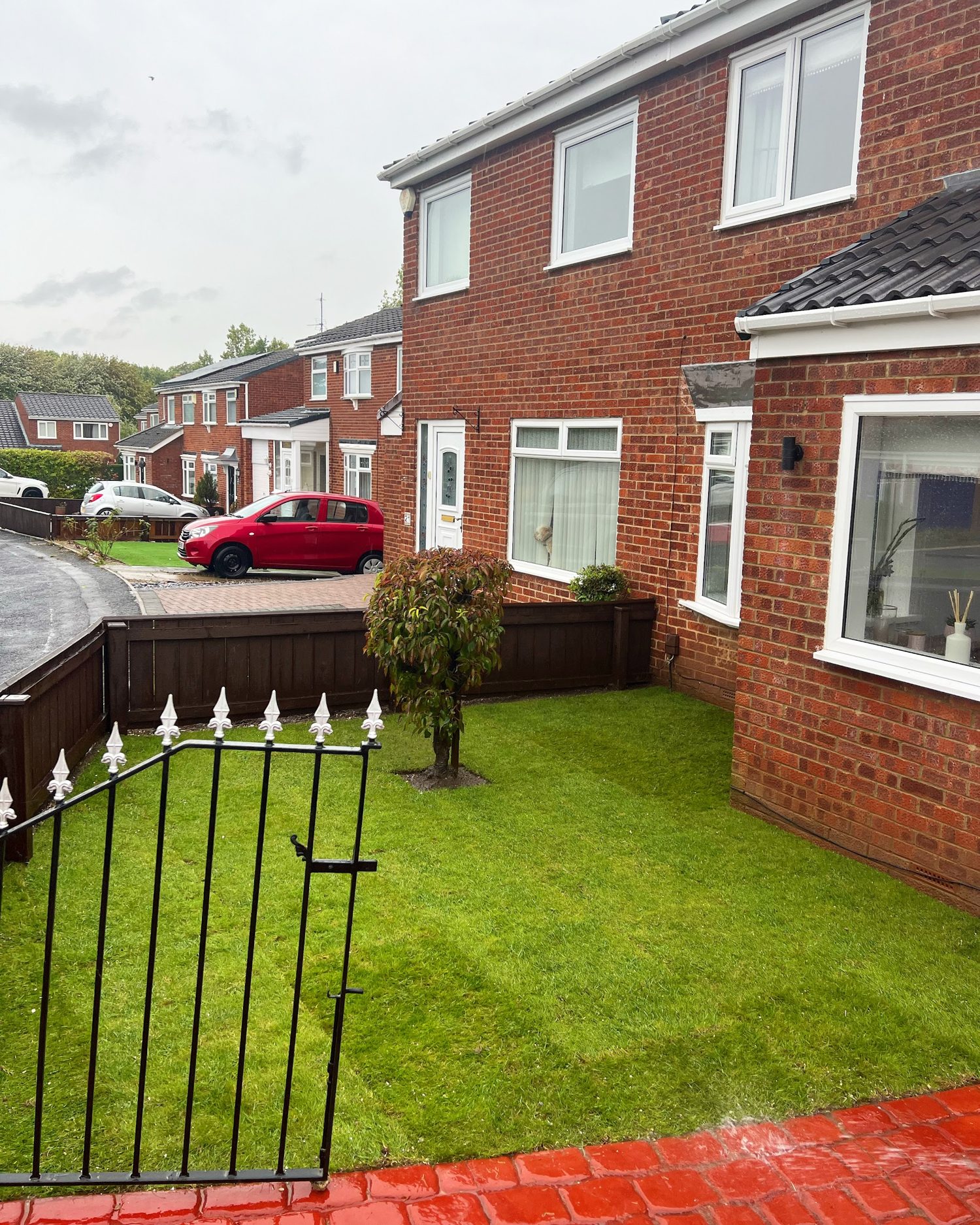 A front garden with fresh turf, a new low wall, black railings and a gate