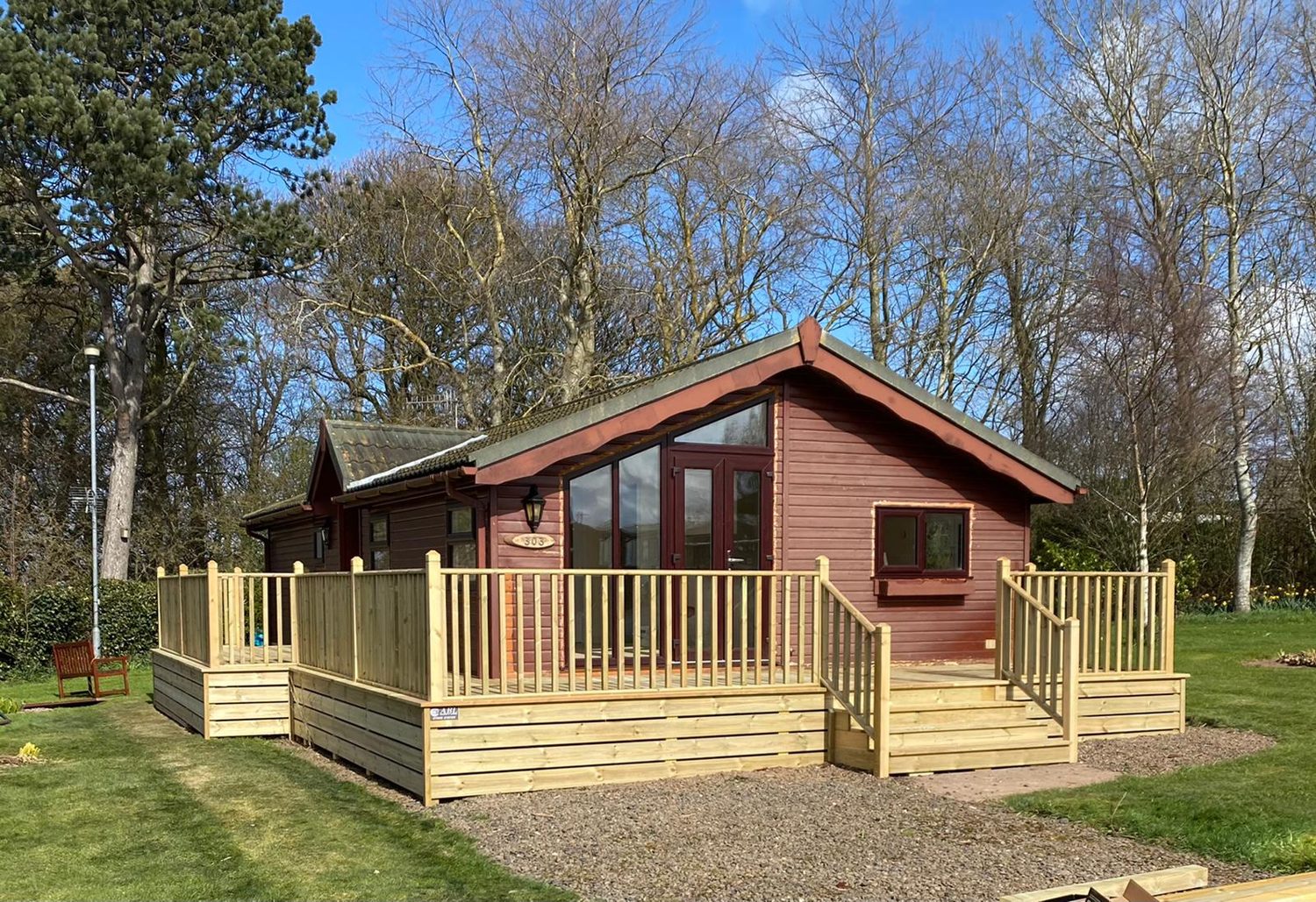 A timber cabin with a decked veranda and balustrade in a park setting