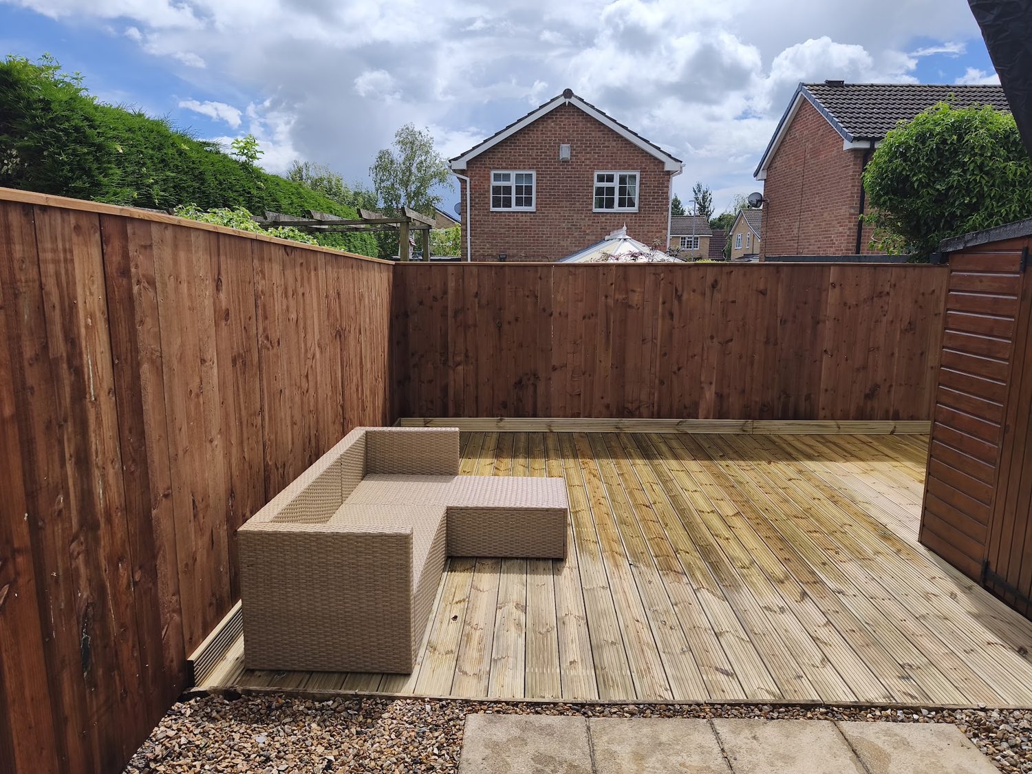 A deck with a rattan corner sofa beside new close-boarded fencing